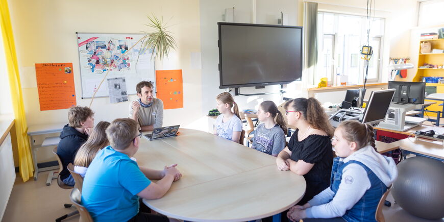 Eine Klasse sitzt mit ihrem Lehrer an einem großen Tisch.