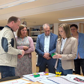 Astrid Wallmann bei ihrem Besuch in der blista: sie hat 3-D-gedruckte Modelle in der Hand, mehrere Personen scheinen im Gespräch mit ihr.