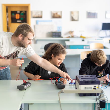Zwei Schül*innen und ein Lehrer im Physikunterricht