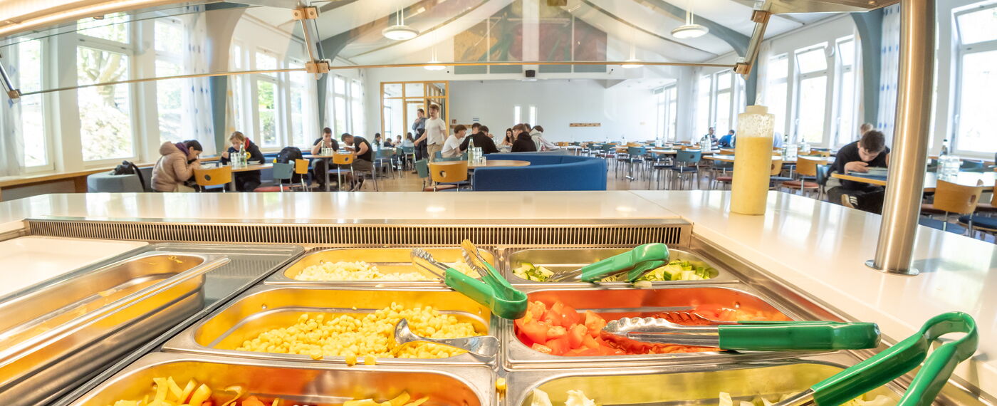 In einem Salatbuffet stehen den Gästen der blista Mensa verschiedene Gemüsesorten zur Verfügung, im Hintergrund ist der Essbereich der Mensa zu erkennen.