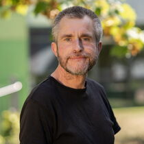 Portraitfoto Frank Hagemann - Er trägt kurze graue Haare und Bart und ein schwarzes T-Shirt.
