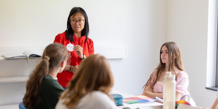Eine Lernbegleiterin hält einen runden Zettel in der Hand, mehrere Schüler*innen schauen zu.