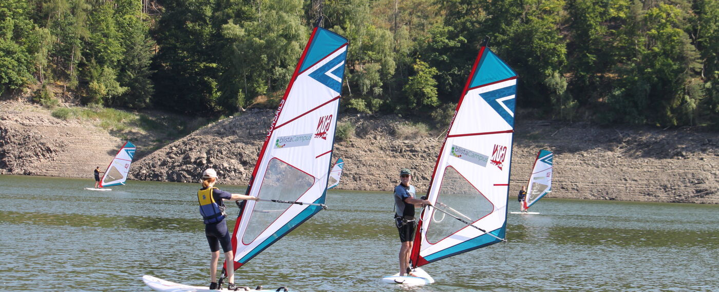Schüler*innen und ein Trainer surfen auf dem Edersee.