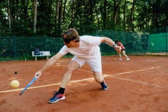 Blindentennis: ein Spieler in Aktion mit Schläger, Ball und Netz