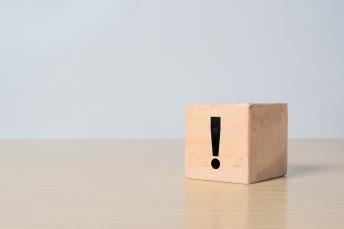 Ein Holzblock mit einem fettgedruckten schwarzen Ausrufezeichen aufgedruckt steht auf einem Tisch