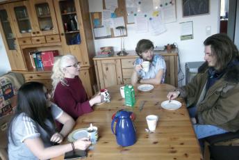 4 junge Leute sitzen bei (den Resten von) Kaffee und Kuchen um einen Tisch