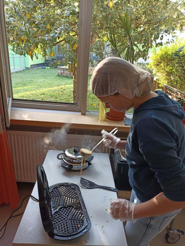 Eine Schülerin füllt Teig mit einer Schöpfkelle in ein Waffeleisen.