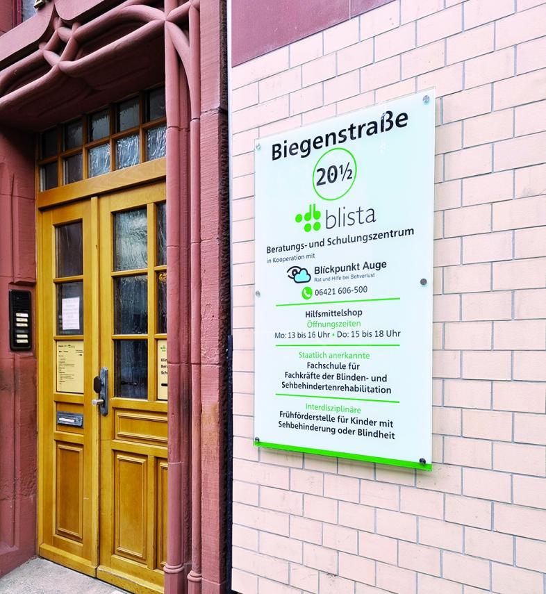 Der Eingangsbereich der Biegenstraße 20 1/2 mit Tür und Schild rechts neben der Tür an der Ziegelwand.
