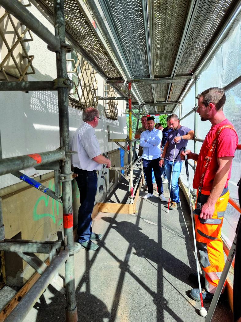 blista-Experte Manfred Fuchs zeigt den Teilnehmenden auf einem eingerüststeten Bürgersteig, wie derartige Baustellen sicher gestaltet werden können.