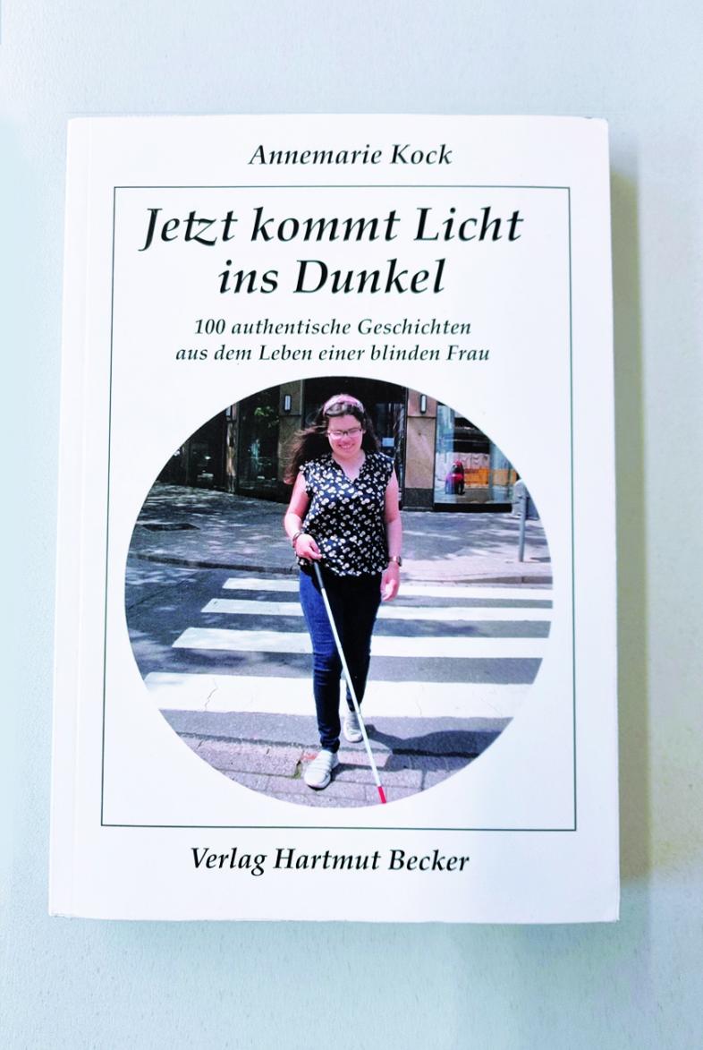 Buchcover von "Jetzt kommt Licht ins Dunkel" von Annemarie Kock. Es ist weiß mit schwarzer Beschriftung hat ein kreisrundes Titelfoto mit einer jungen Frau, die mit Langstock einen Zebrastreifen überquert.