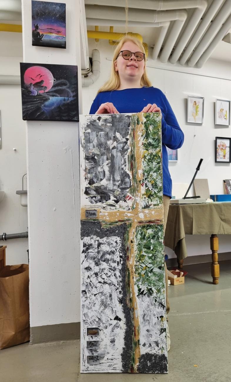 Lisa Sosnowski hält ihr großformatiges Gemälde im Malatelier in die Kamera. Auf den Boden aufgestellt ist es etwa brusthoch und etwas breiter als sie.
