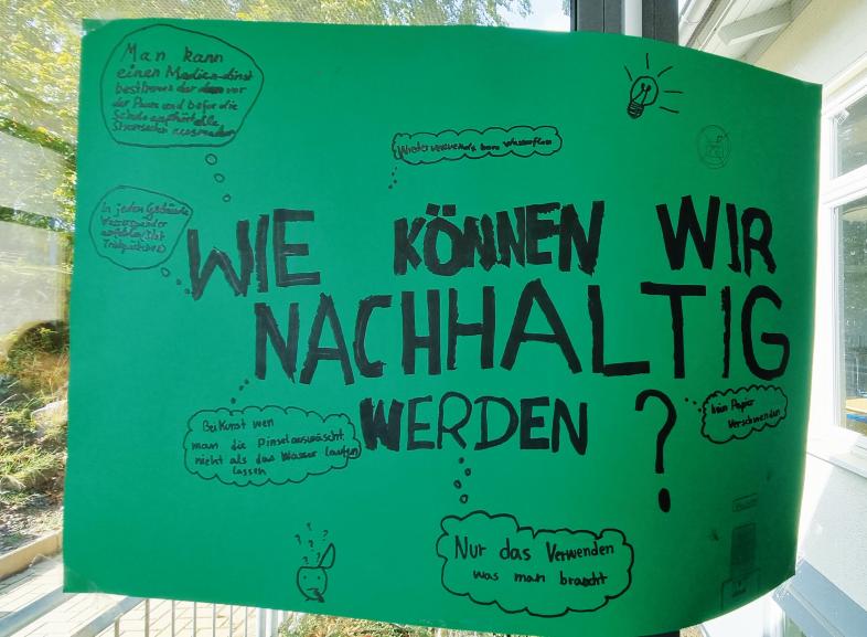 Foto eine grünen Plakates, das in großen Druckbuchstaben in der Mitte fragt: "Wie können wir nachhaltig werden?" Ideen dazu sind in Denkblasen außenrum geschrieben.