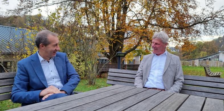 Patrick Temmesfeld (links im Foto) und Maarten Kubeja (rechts) sitzen über Eck an einem Tisch im Freien und unterhalten sich angeregt. Beide wirken vergnügt.