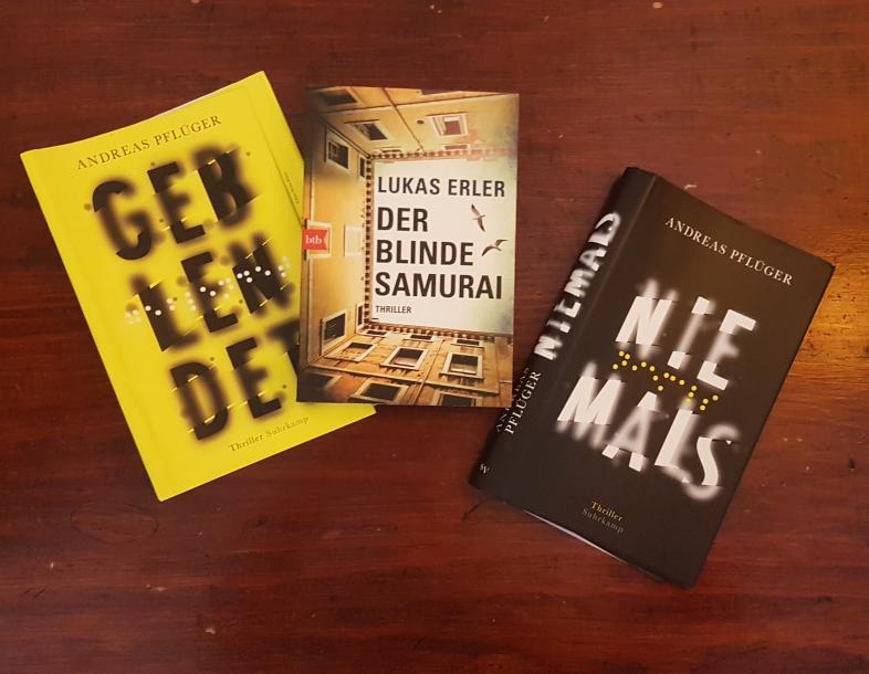 Auf einem Holztisch liegen mehrere Bücher: „Geblendet“, „der blinde Samurai“ und „Niemals“.