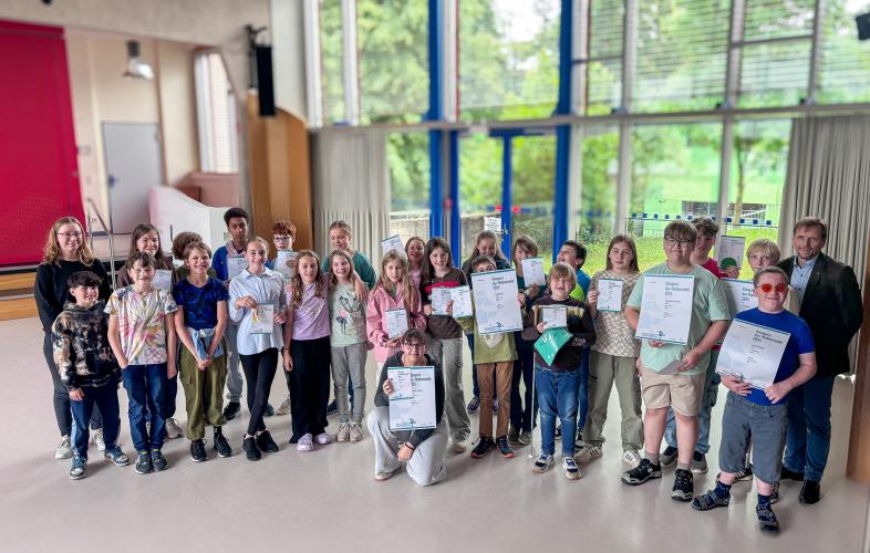 Gruppenbild: Stolz halten die Schüler*innen ihre Urkunden in der Hand, links Debora Ziemann, rechts Peter Audretsch 