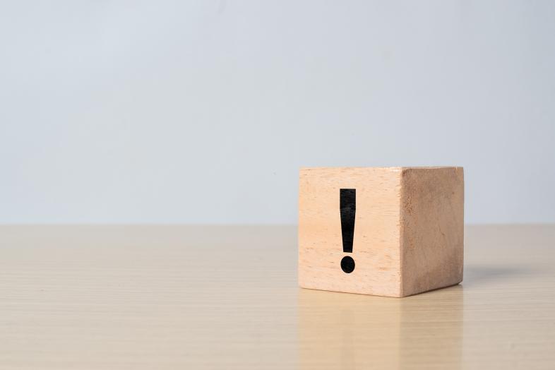 Ein Holzblock mit einem fettgedruckten schwarzen Ausrufezeichen aufgedruckt steht auf einem Tisch