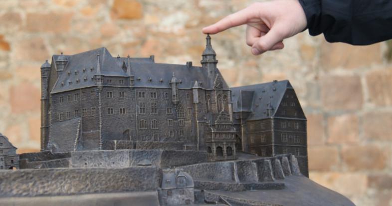 Eine Hand zeigt mit dem Zeigefinger auf das taktile Marburger Schloss-Modell
