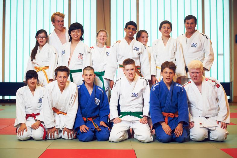 Das Foto zeigt eine der blista-Judoka-Gruppen: 13 Mädchen und Jungen in blauen und weißen Anzügen mit ihrem Trainer