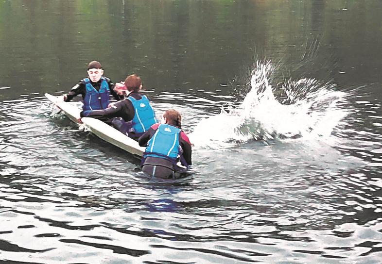 Vier Schüler*innen in Neoprenanzügen und mit Schwimmwesten fallen von einem Stand-Up-Board ins Wasser.
