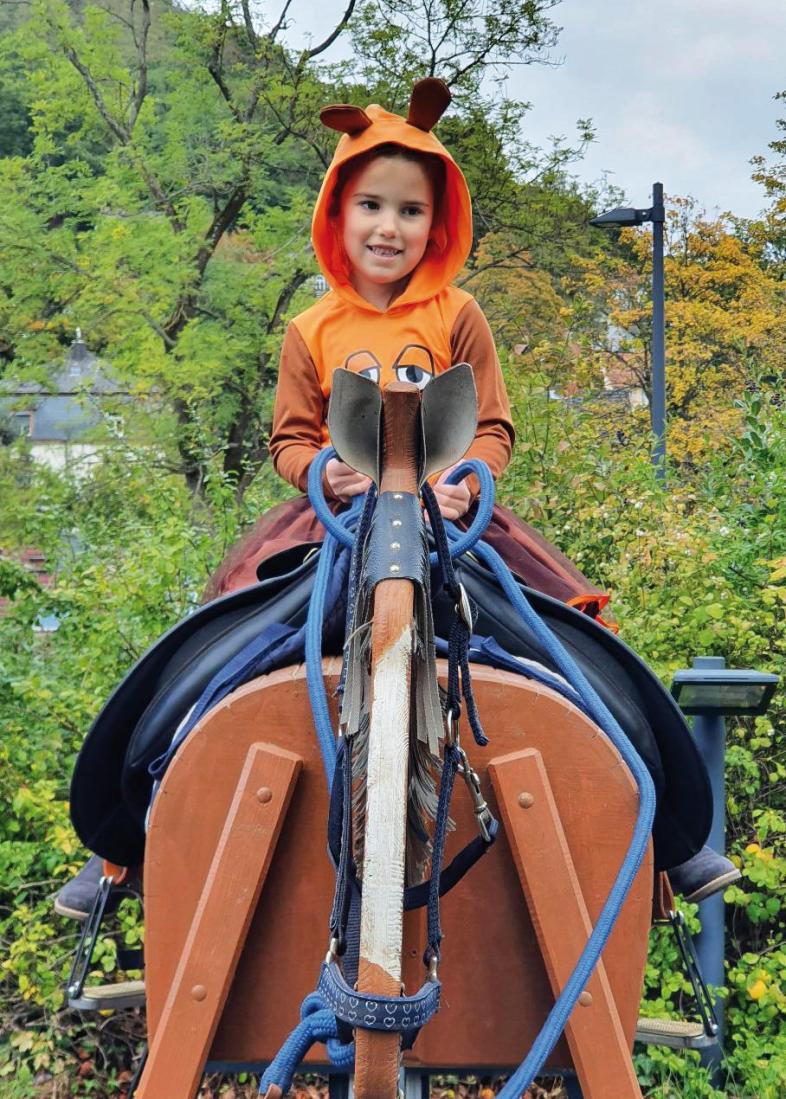 Bild 4: Ein Kind mit Mauskostüm sitzt perfekt auf dem Rücken des Holzpferdes. Es hält die Zügel locker und hat die Füße in den Steigbügeln.