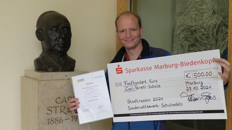 Dr. Tobias Mahnke, Lehrer an der Carl-Strehl-Schule präsentiert einen übergroßen Scheck über 500 € und die Urkunde vom Stadtradeln.