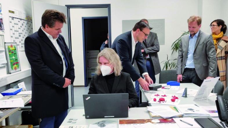 Die Leiterin der Deutschen Blindenbibliothek, Andrea Katemann, zeigt Herrn Dusel etwas am Laptop. Im Hintergrund betrachtet Sören Bartol 3D-Modelle für den Unterricht.