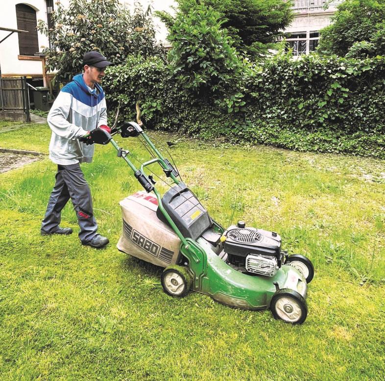 Ein junger Mann mäht den Rasen mit professionellem Gerät