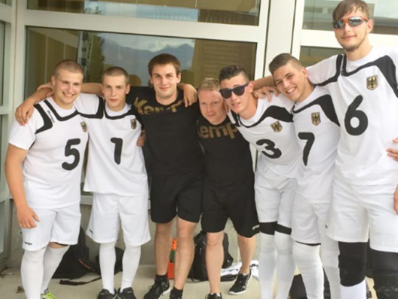 Fünf Goalballer in weißen Trikots und zwei Trainer in schwarz lachen in die Kamera