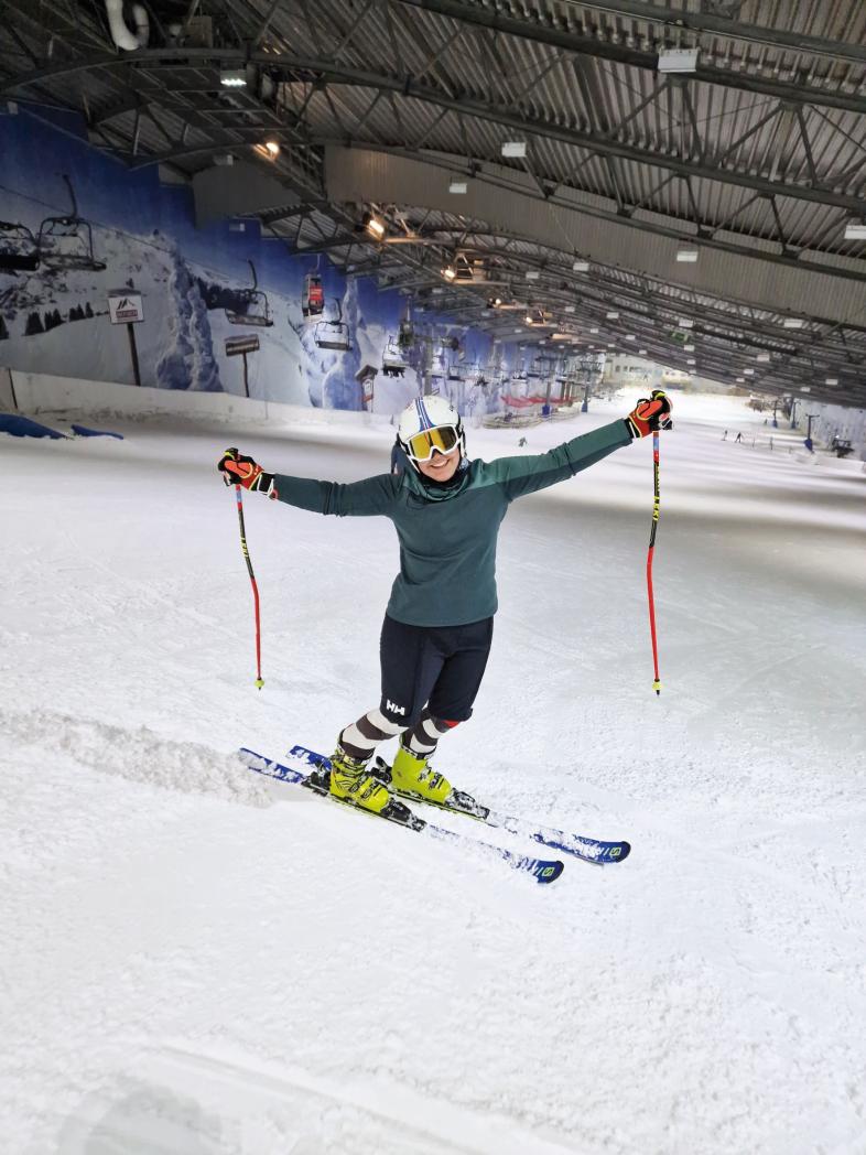 Hanna Gieg steht auf Skiern in einer Indoor-Skihalle und hebt beide Arme mit den Stöcken an.