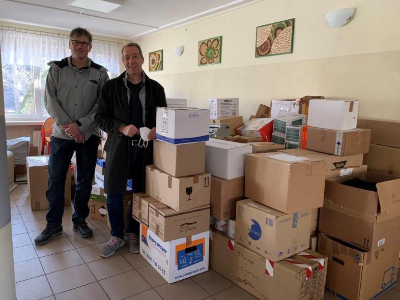 Zwei Personen stehen vor mit Hilfsmitteln befüllten Kisten