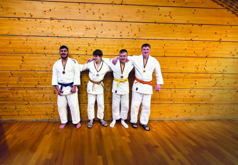 .Vier junge Männer stehen mit weißen Judoanzügen in einer Sporthalle, sie tragen Medaillen um den Hals.