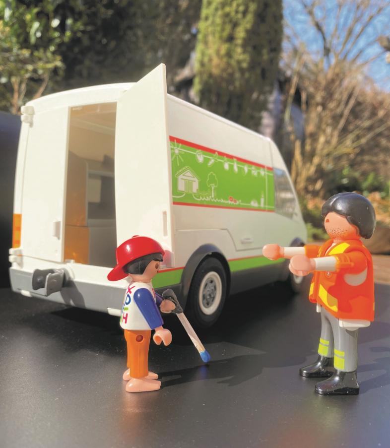 Mit Playmobil nachgestellte Szene: ein Kind mit roter Basecap und Langstock stößt an die offene Hecktüre eines Transporters. Gegenüber von ihm steht ein Erwachsener mit orangener Warnweste und streckt ihm beide Arme entgegen. 