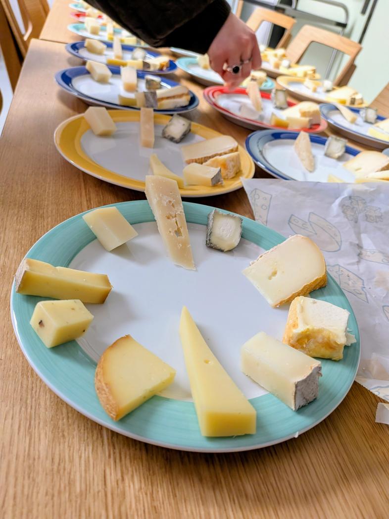 Eine Mitarbeiterin von Wein und Käse richtet 10 verschiedene Käsesorten auf einem Teller an.