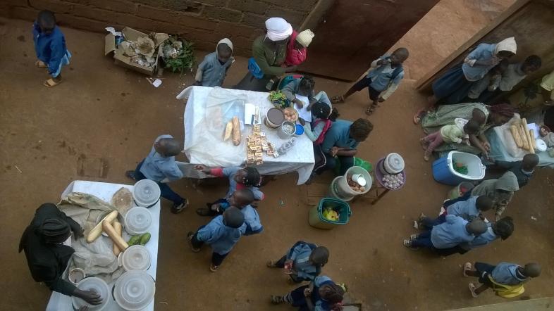 Ein Blick von oben auf den Schulhof: Kinder in blauer Schuluniform laufen über lehmigen Boden.