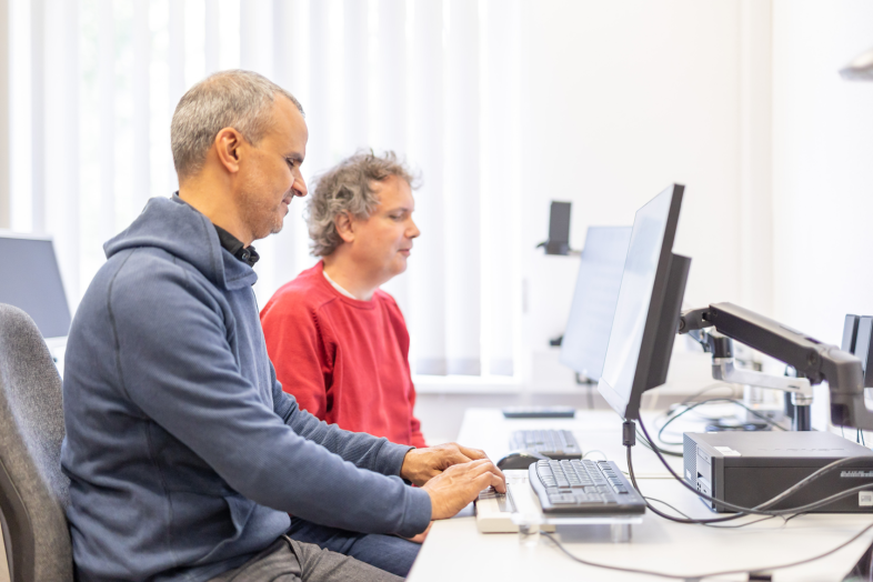 Zwei Männer arbeiten an einem blindenspezifisch ausgestatteten PC-Arbeitsplatz