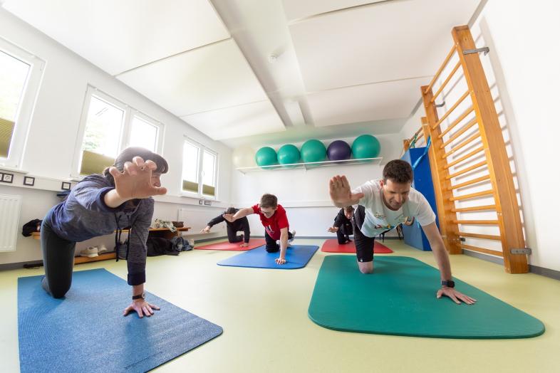 Vier Personen knien auf Gymnastikmatten in einem Sportraum und führen eine Übung im Vierfüßlerstand aus.