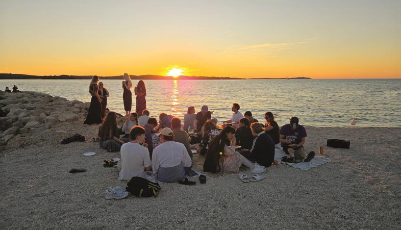 Traumhafte Aussicht am Abend, die Gruppe trifft sich zu einem Picknick am Strand, während die Sonne über der Adria untergeht.