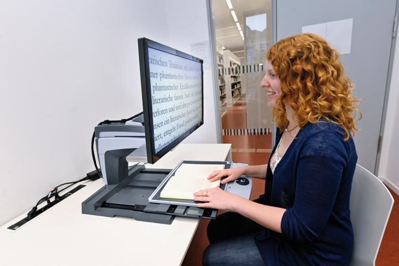 Eine Studentin mit Sehbehinderung liest mit dem Bildschirmlesegerät ein Buch.