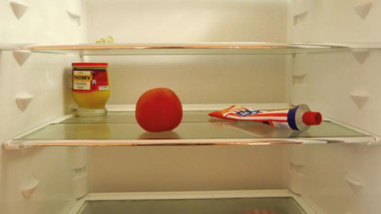 Ein Blick in den fast leeren Kühlschrank, man sieht einen Apfel, ein Glas Senf und eine Tube