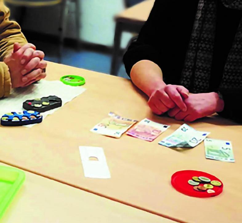 Bild von den Händen zweier Personen, die Gschein und Münzen mit verschiedenen Gelderkennungshilfsmitteln vor sich auf dem Tisch liegen haben.