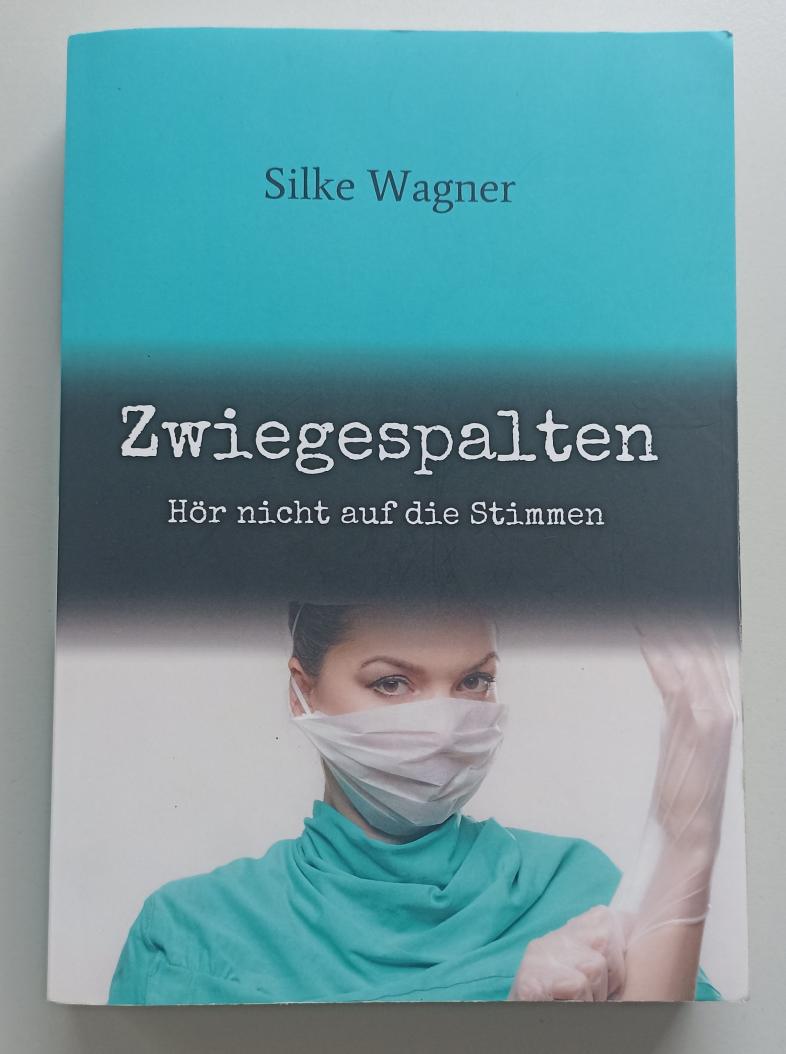 Buchcover von Zwiegespalten von Silke Wagner. Eine Frau mit Mundschutz, Handschuhen und OP-Kleidung schaut in die Kamera.