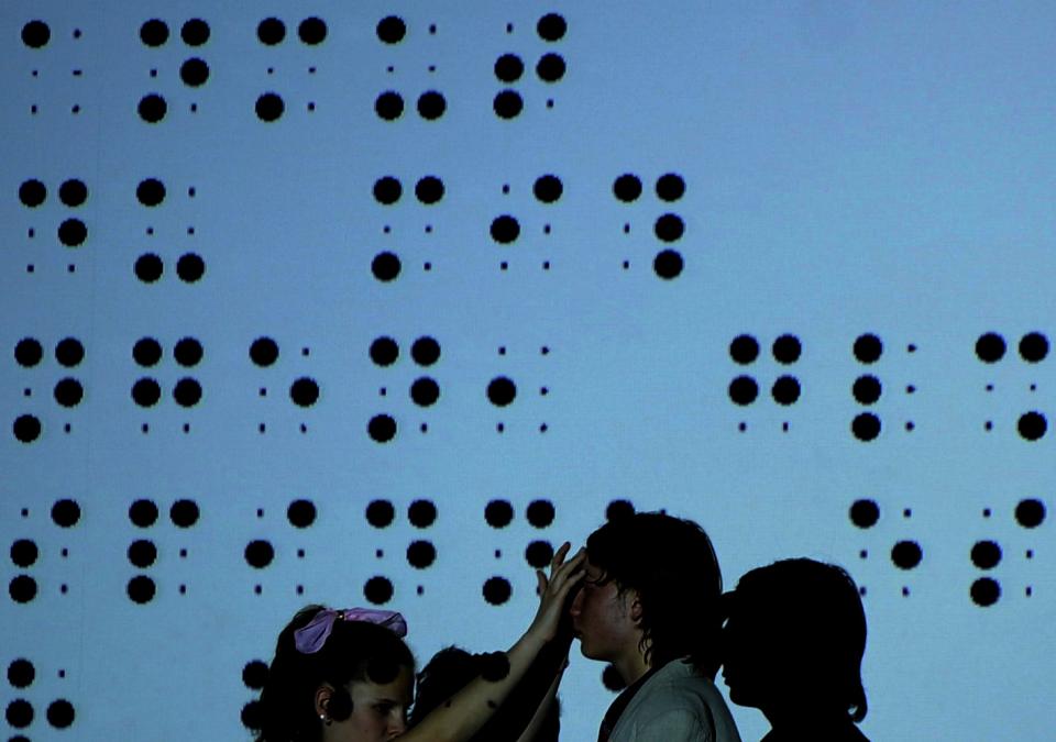 Bild 10 von 13: Zwei Schattenfiguren vo einem überdimensionalen Bild der Blindenschrift Braille