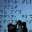 Zwei Schattenfiguren vo einem überdimensionalen Bild der Blindenschrift Braille