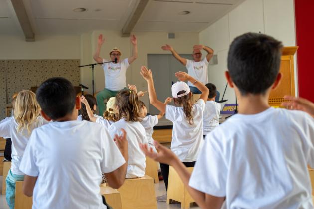 Kinder sitzen auf Cajons trommeln und strecken die Hände in die Luft. Auf der Bühne geben zwei Männer auf Cajons den Takt vor.