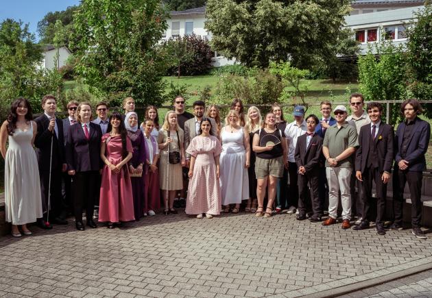 Die Absolvent*innen der CSS stehen festlich gekleidet auf dem sonnigen Campus.
