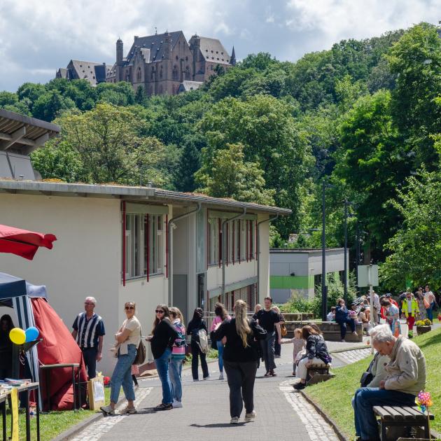 Auf dem blista Sommerfest ist der Campus mit vielen Menschen bevölkert - im Hintergrund das Marburger Schloss.