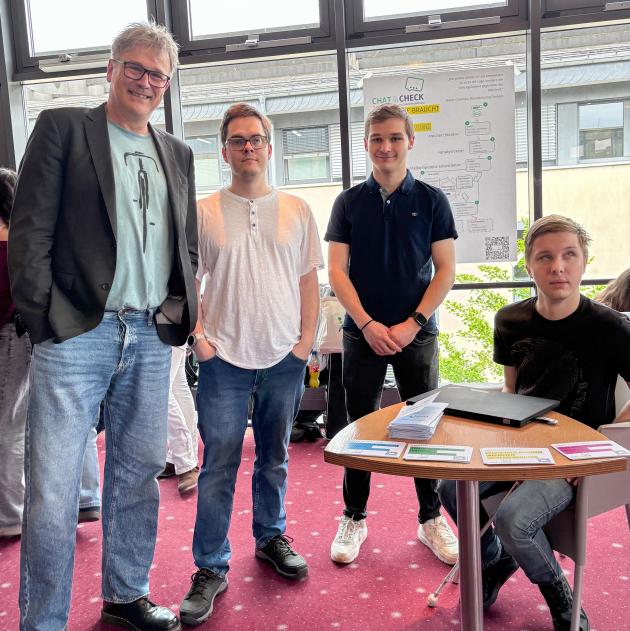 Otfrid Altfeld steht mit den drei Preisträgern im Cineplex vor einem Plakat, das über ihr Projekt informiert. 