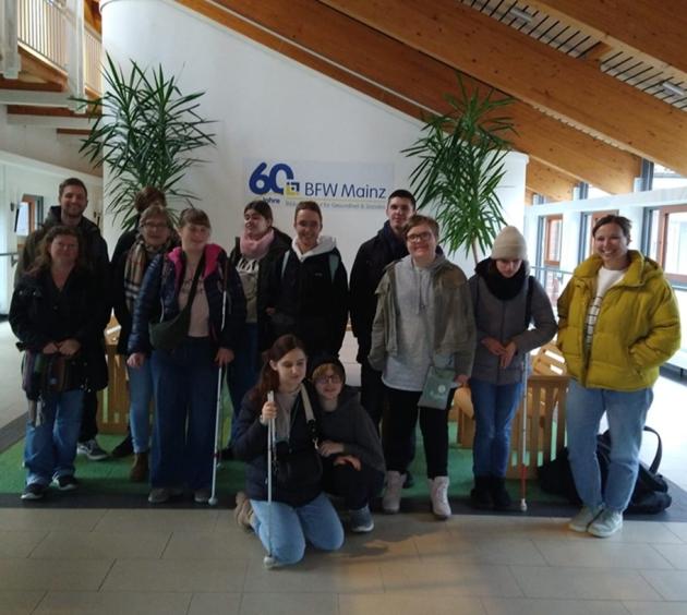 Gruppenbild der gutgelaunten FOS Klasse mit ihren Lehrerinnen vor einem Banner "60 Jahre BFW Mainz