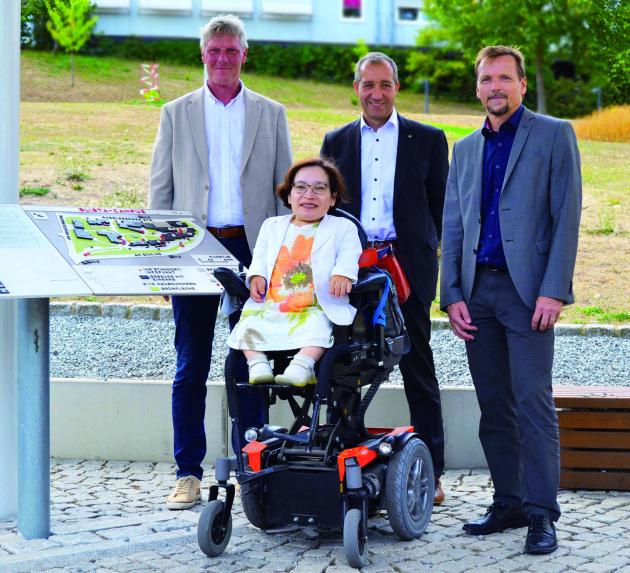 Maarten Kubeja, Patrick Temmesfeld und Peter Audretsch stehen hinter Rika Esser, die in einem Rollstuhl neben dem Infopoint auf dem blista-Campus sitzt.