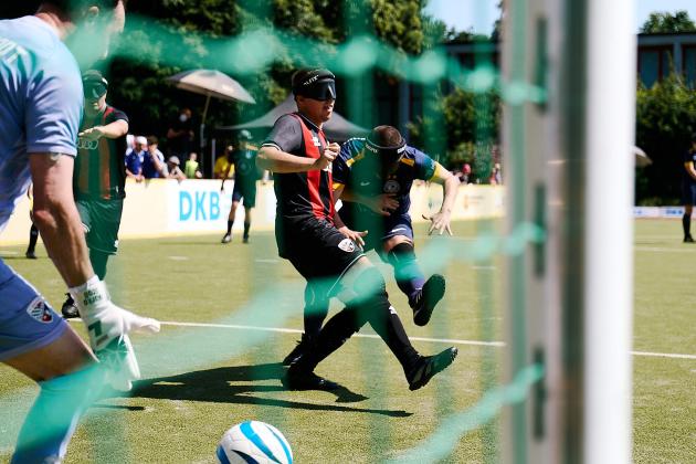 Blick durch ein Tornetz im Blindenfußball, Zwei Spieler im Duell, einer schießt den Ball in Richtung Tor.